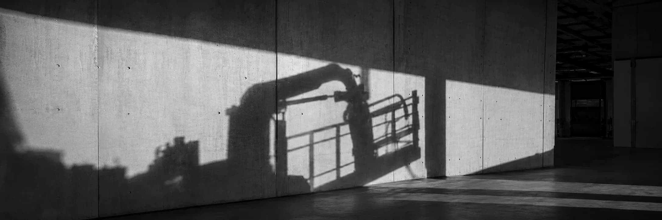 Shadow of an industrial robot arm cast across a concrete factory wall